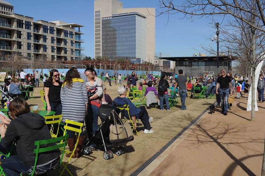 Many people on chairs and standing talking in a park with buildings behind, at Klyde Warren Park in Dallas